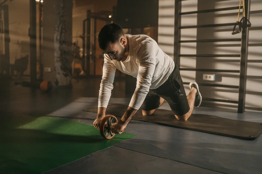 Exercices d'un homme fort utilisant une roue abdominale sur le sol dans une salle de sport sombre seul