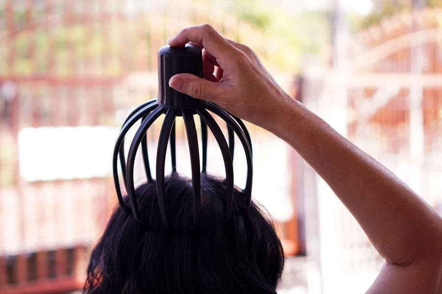 The picture shows a demonstration of using a portable head massage device powered by a battery for relaxing massage and improving blood circulation in the skull.