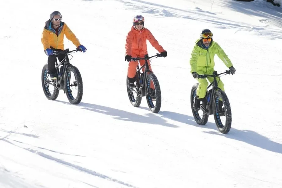 Três pessoas andando de bicicleta na neve com roupas refletivas