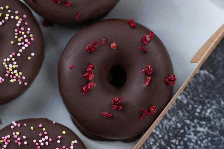 süße leckere Donuts in Schokoladenglasur mit vielen Streuseln überzogen in einer Schachtel