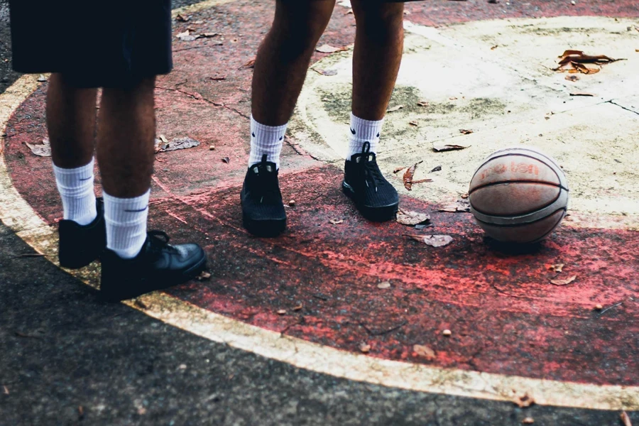 Zwei Personen in schwarzen Schuhen stehen auf Betonboden neben einem Basketball