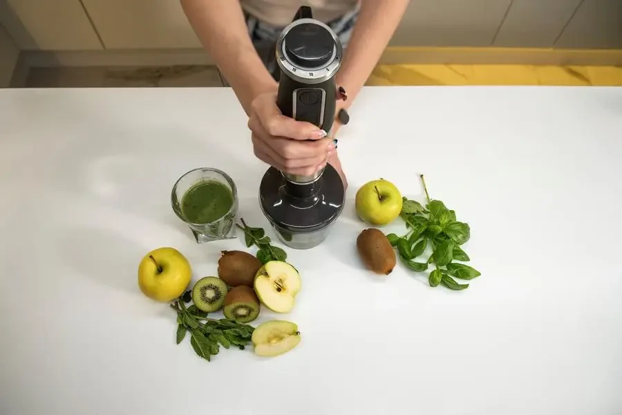 Young woman with hand blender making smoothie for breakfast in kitchen