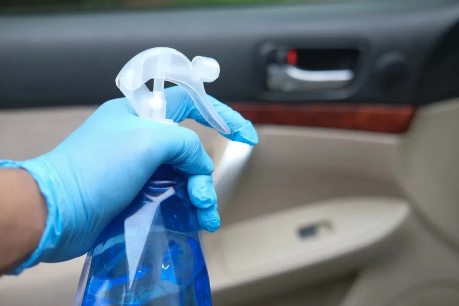 mano en guantes sosteniendo una botella de spray limpiando la puerta del auto