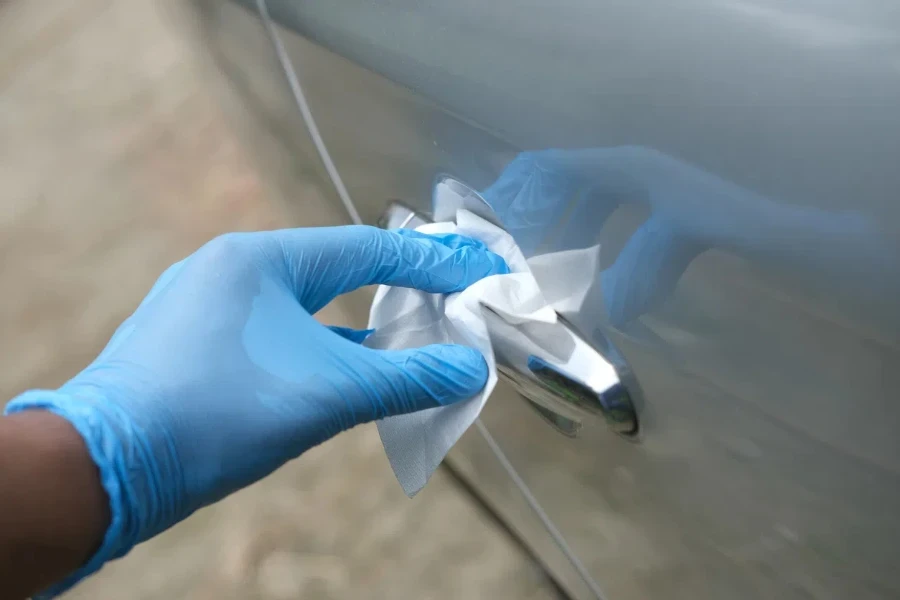 mano en guantes sosteniendo una botella de spray limpiando la puerta del auto