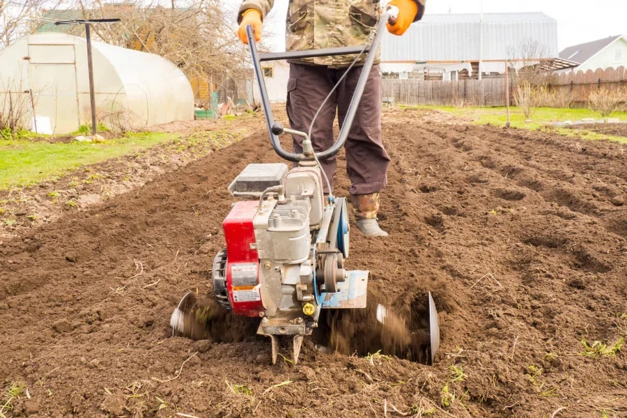 um homem trabalha a terra no jardim com um cultivador