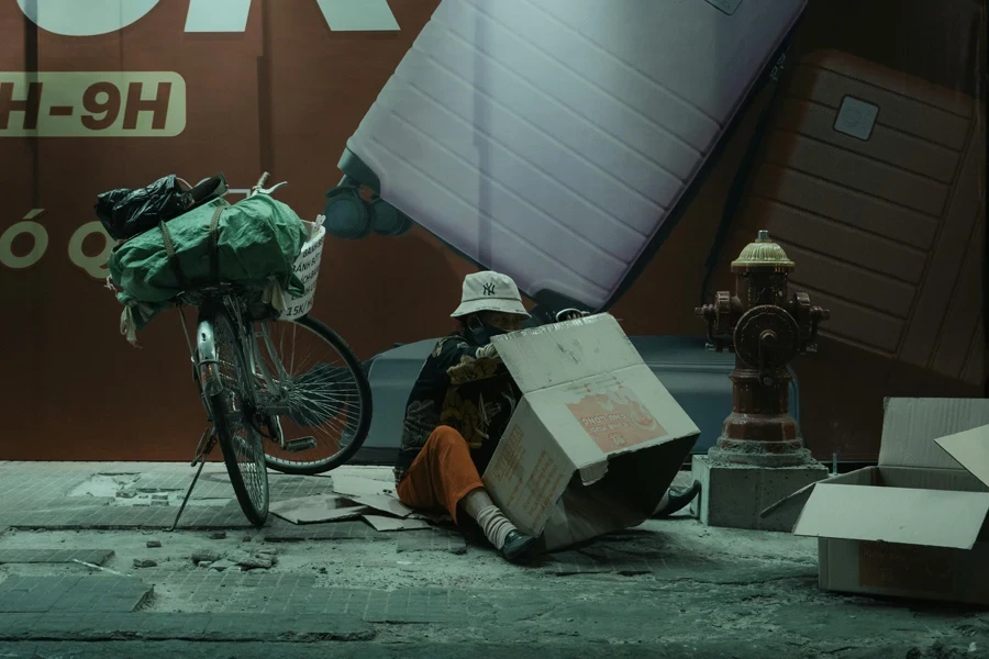 A Person Sitting on the Pavement with a Cardboard Box