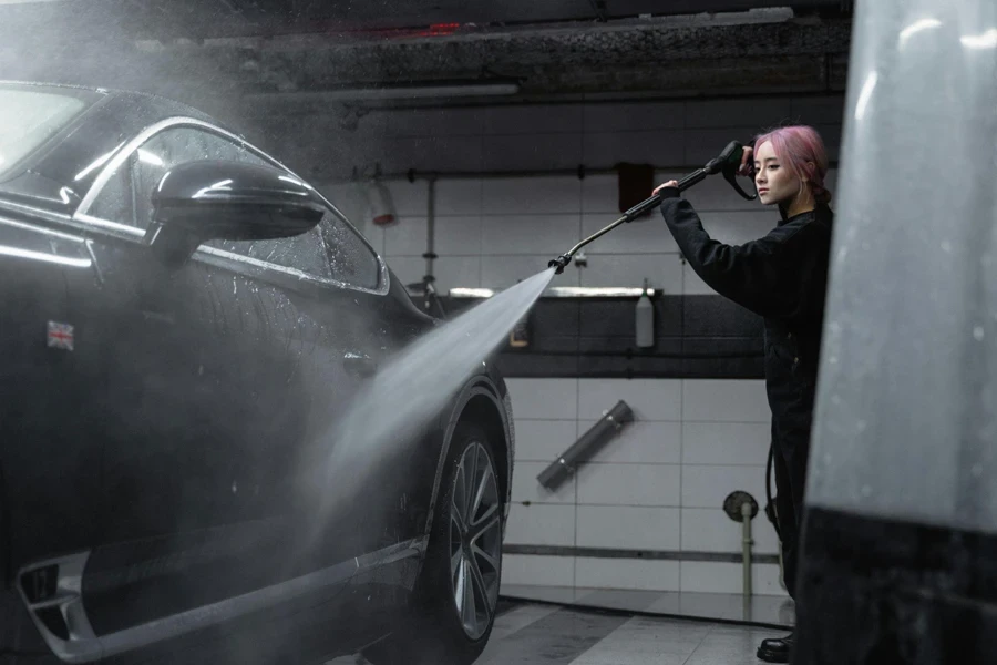 Une femme nettoie la voiture noire à l'aide d'un tuyau de lavage à pression