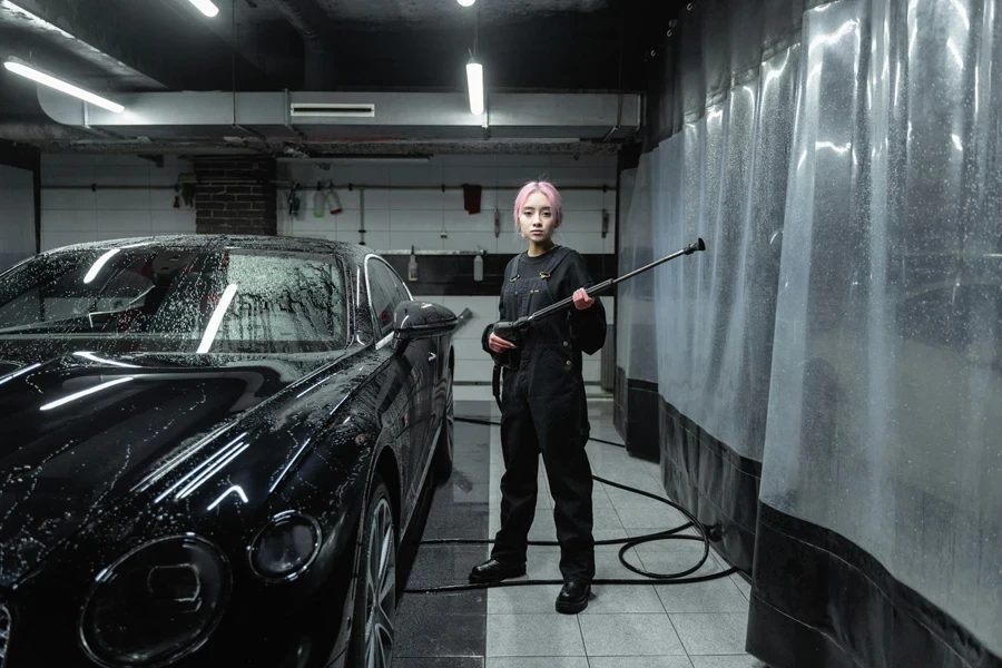 A Woman Holding a Hose Standing Beside a Black Car