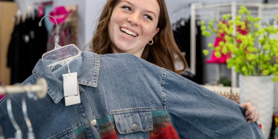 A smiling, energetic young woman holds up a new denim jacket