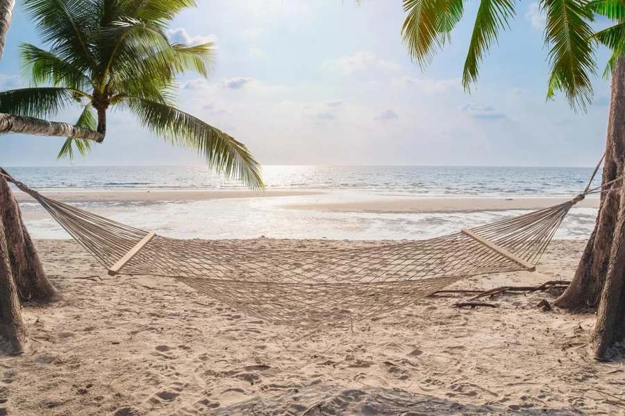 A white cradle surrounded by trees in a sand field on a seashore on a summer day with a clear sky