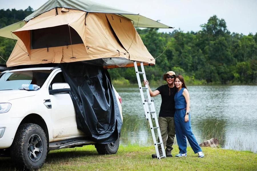 Coppie asiatiche che si rilassano con il camper della tenda sul tetto vicino al fiume