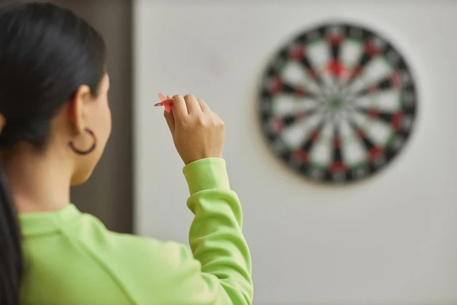 Back view closeup of young woman playing darts and aiming shot