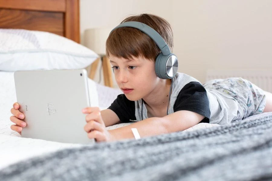 Boy wearing headphones watching content on a tablet in bed