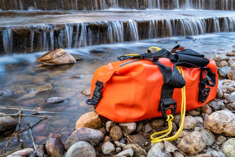 Leuchtend orangefarbener, wasserdichter Seesack neben einem kleinen Wasserfall