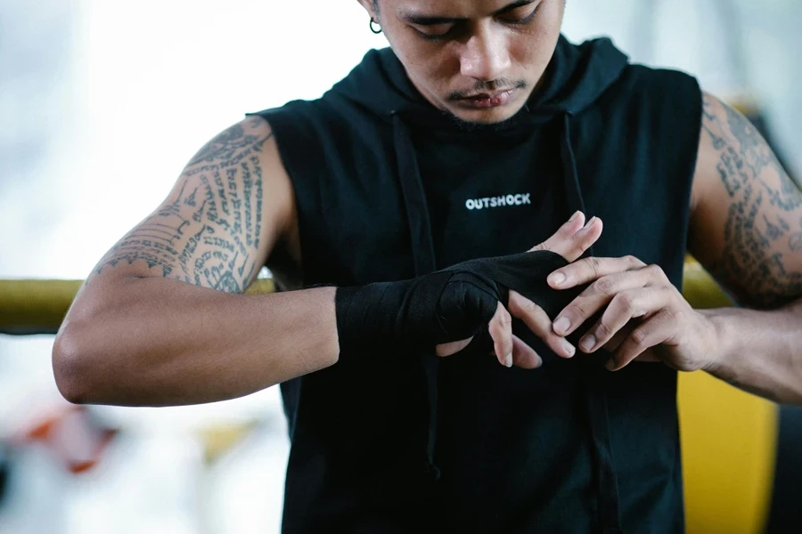 Brutal ethnic boxer bandaging hand in gym