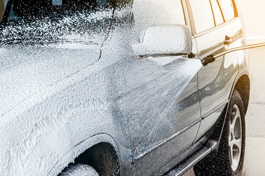 Car exterior covered with layer of soft foam and foam spraying from hose