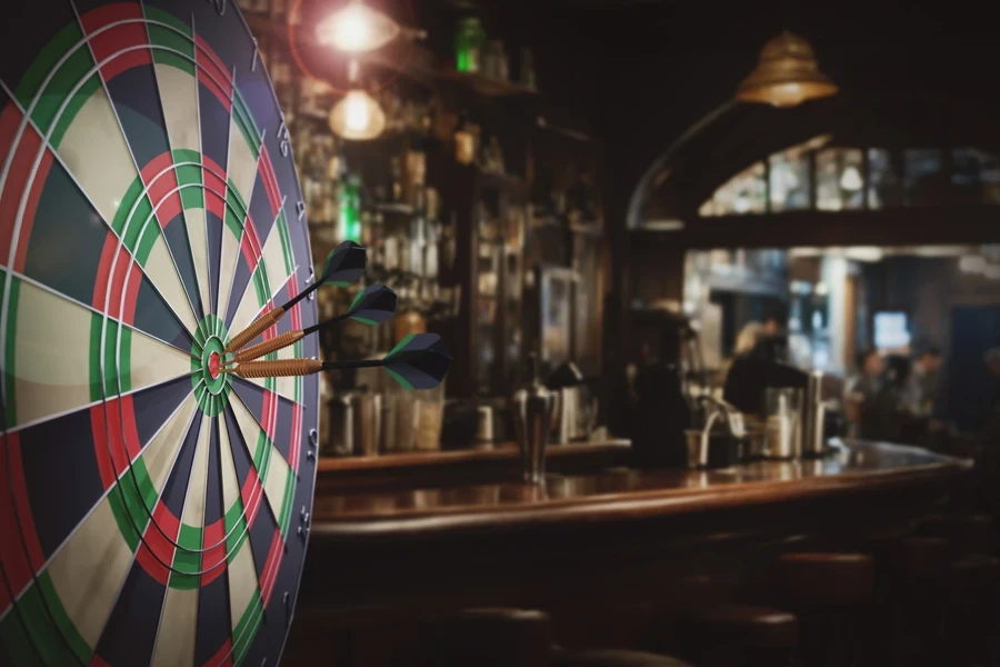 Dart board with three darts outdoors white blured bar background