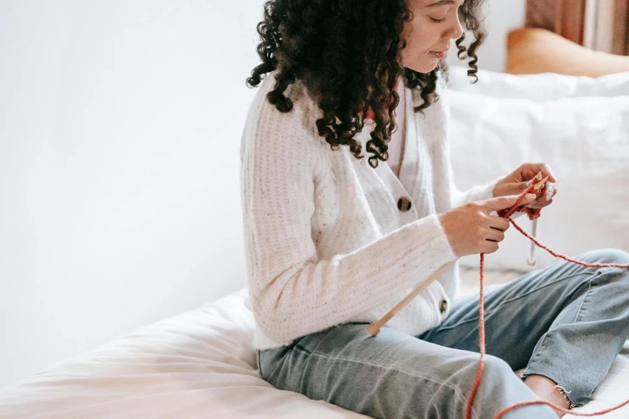 Donna concentrata che lavora a maglia con aghi e filati seduta sul letto