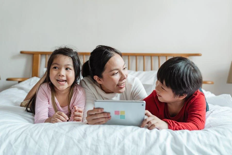 Mother using tablet with kids on bed