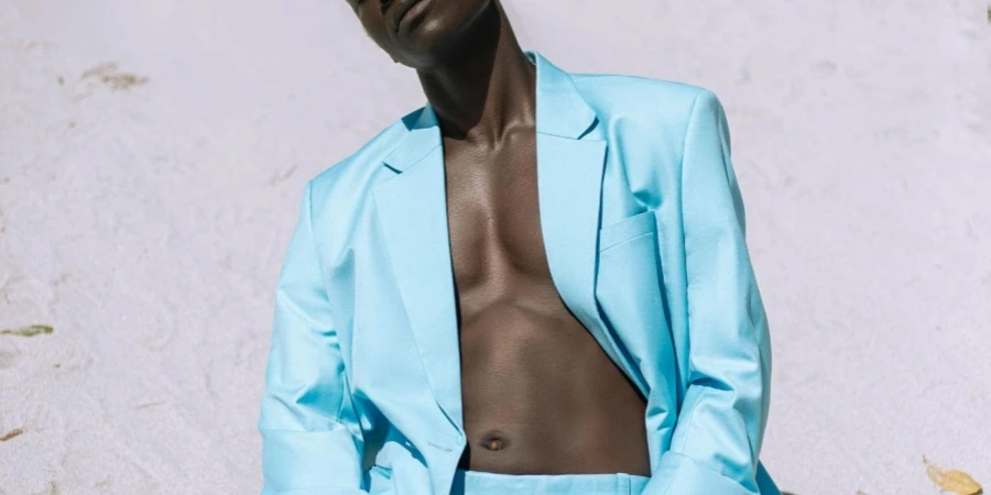 Man zonder shirt in blauw jasje en broek knielend op zand