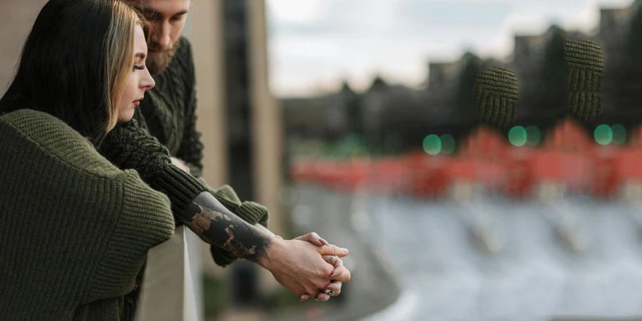 Seitenansicht eines Hipster-Mannes mit einer charmanten jungen Geliebten, die auf einem Balkon in der Stadt Händchen hält