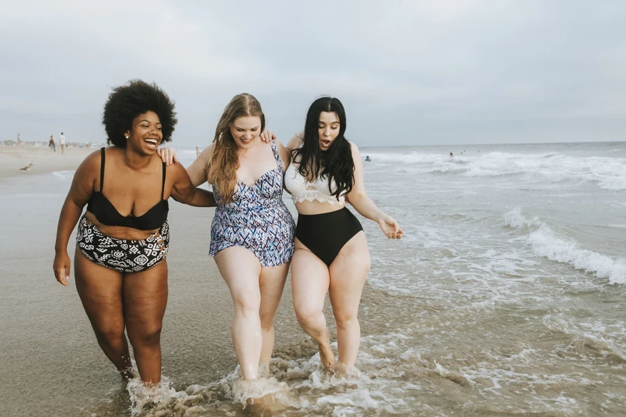 Two women in two-piece swimwear and one in a swim dress