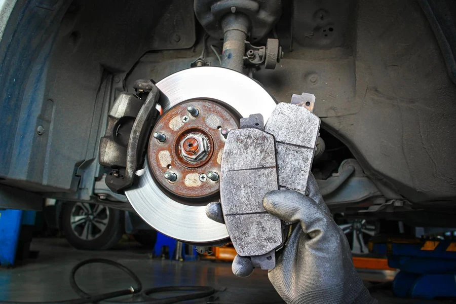 Used car brake pads in the hands of a mechanic with brake discs and brake calipers