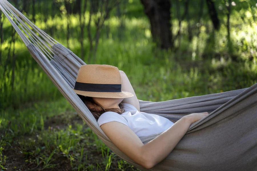 Woman resting in a hammock in a summer garden covering her face with a straw hat