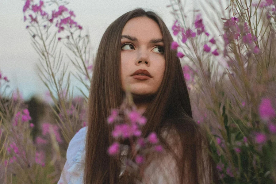 Young Beautiful Woman Standing among Blooming Flowers in Meadow