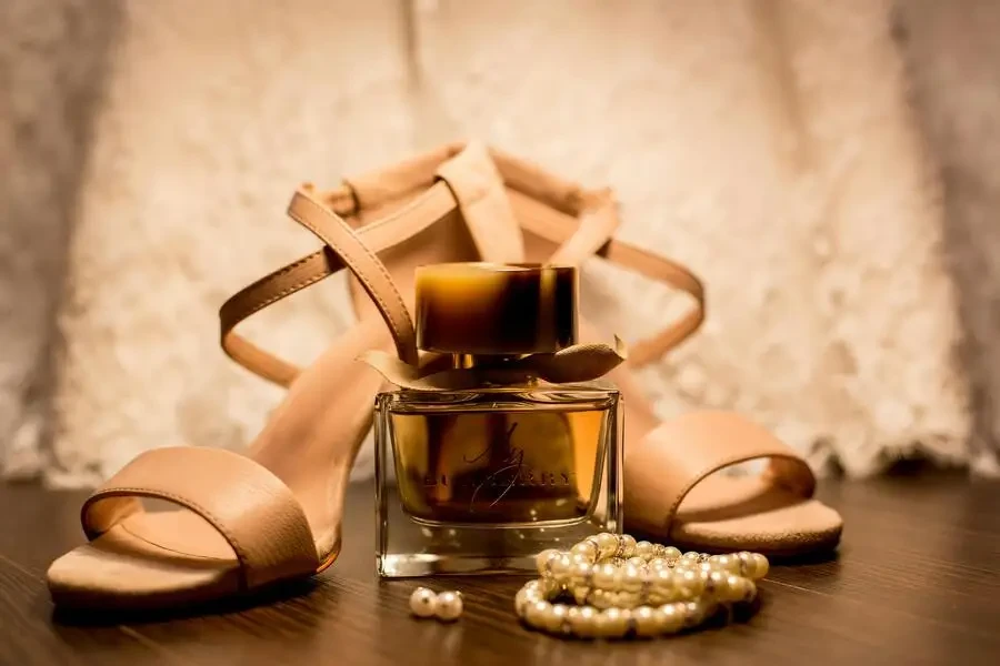 سوار من اللؤلؤ الأبيض بجانب حذاء بني وعطر