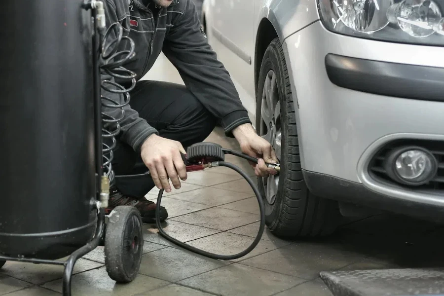 Hombre de chaqueta negra bombeando un neumático de coche