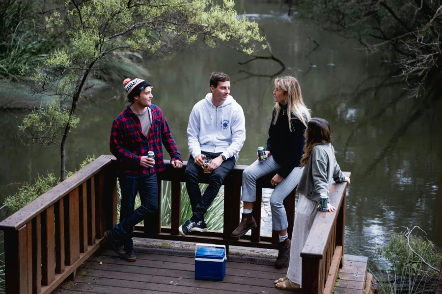 Um grupo de pessoas em um deck de madeira perto do lago bebendo cerveja