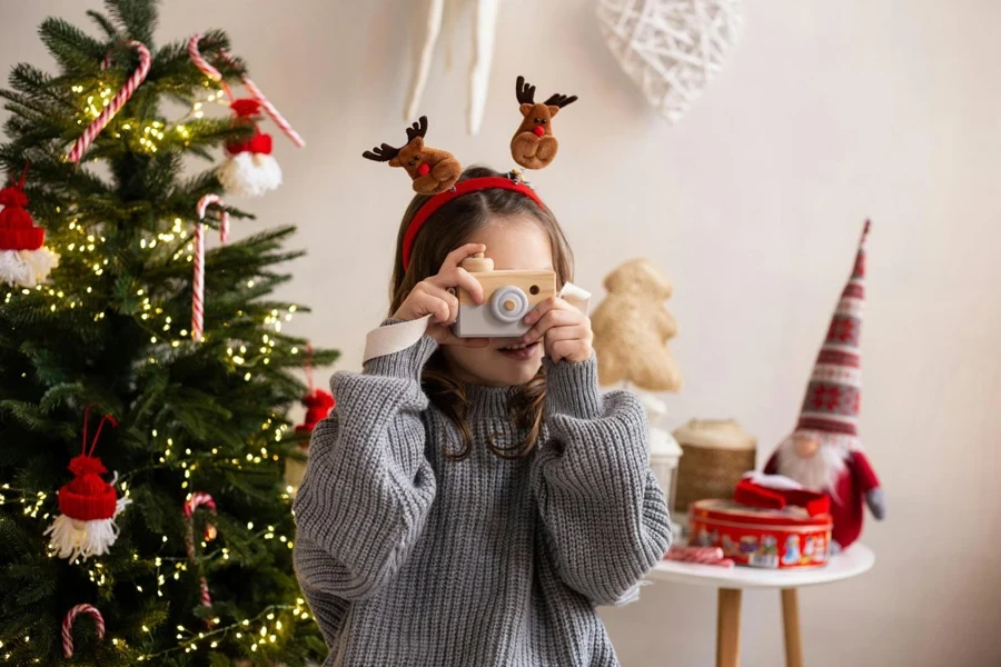 Ein junges Mädchen mit einer Spielzeugkamera vor dem Weihnachtsbaum