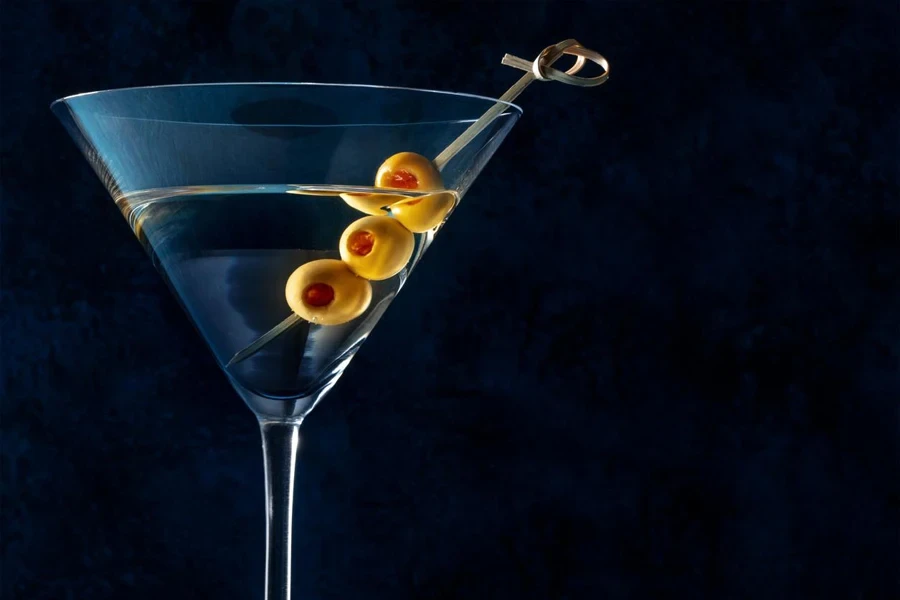 A glass with spicy olives on a toothpick on a dark background