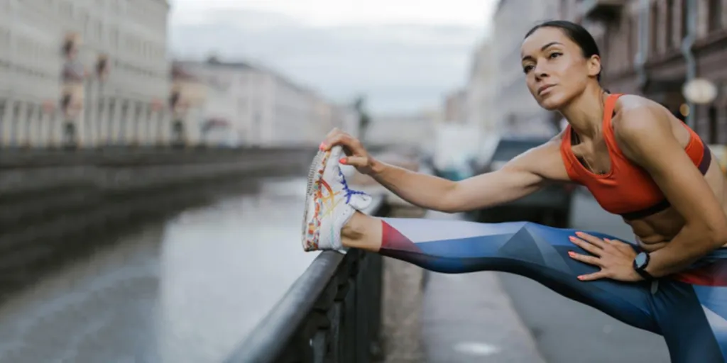 Uma mulher vestindo leggings e sutiã esportivo enquanto estica as pernas