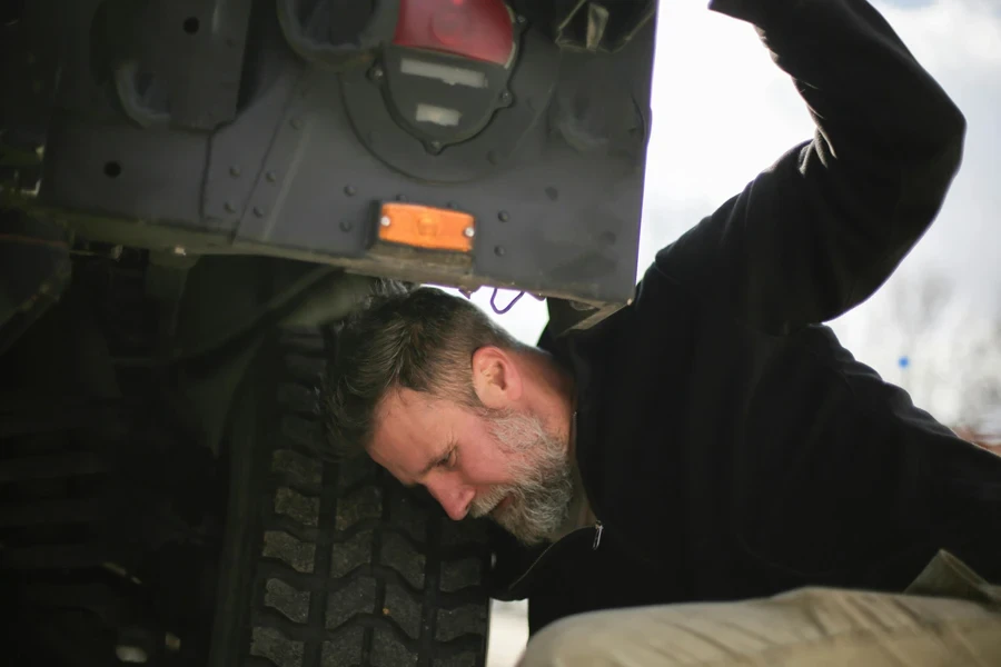 Adult bearded mechanic fixing car wheel on street