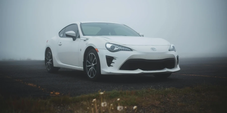 Asphalt road in green field with parked modern white automobile in foggy weather