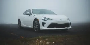 Strada asfaltata in un campo verde con un'automobile bianca moderna parcheggiata in un clima nebbioso