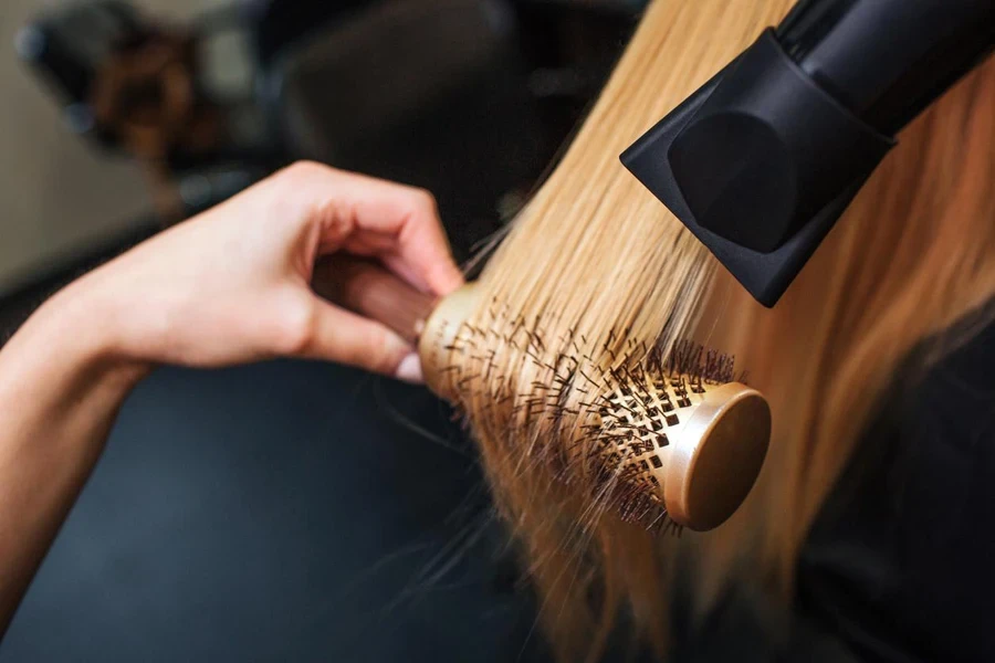 Close-up of hairdresser hands drying blonde hair with hairdryer and round brush