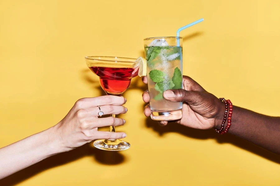 Close-up of multiethnic couple clinking cocktails against yellow background