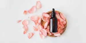 Flacon cosmétique dans une assiette en bois à côté de pétales de rose roses