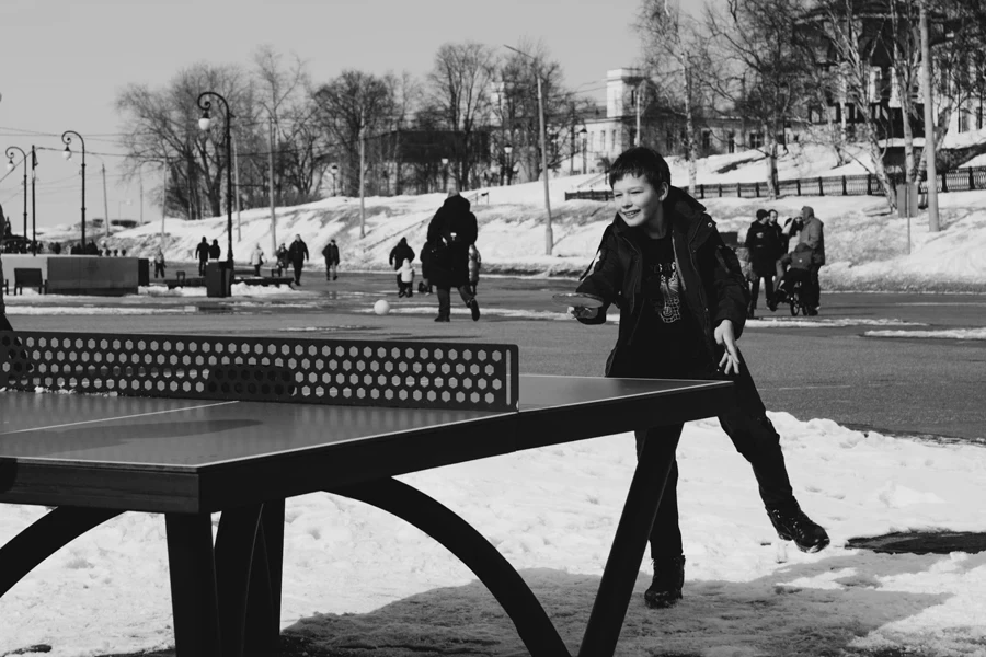 Foto em tons de cinza de um menino jogando tênis de mesa