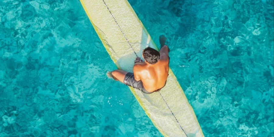 Mann sitzt auf Surfbrett