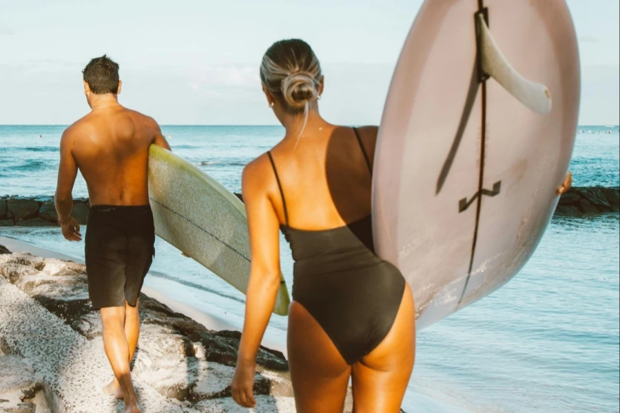 Uomo e donna che trasportano tavole da surf mentre camminano