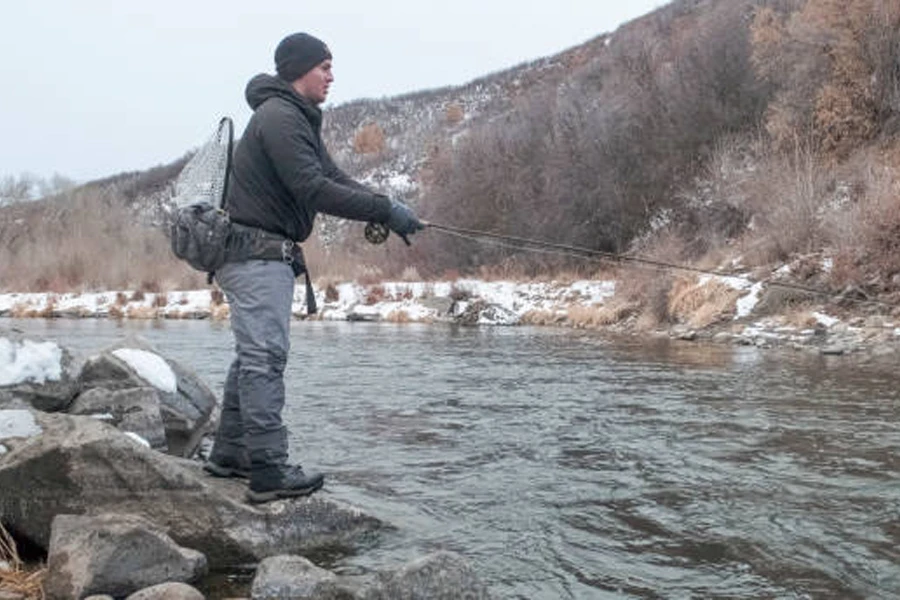 Homem pescando ao longo do rio no inverno com calças e botas