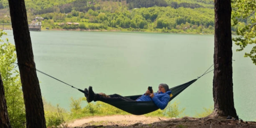 Man in a Hammock Reading a Book on a Tablet