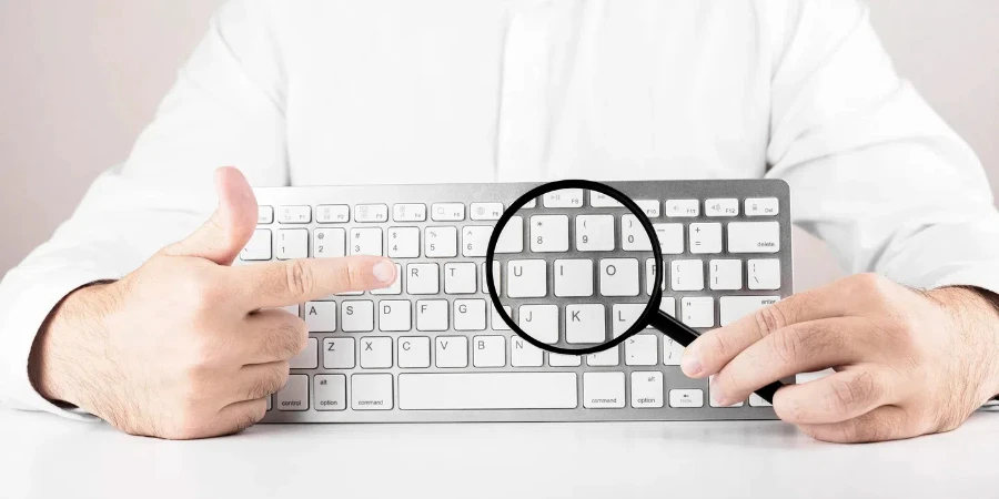 Man with magnifying glass and white keyboard of computer or laptop