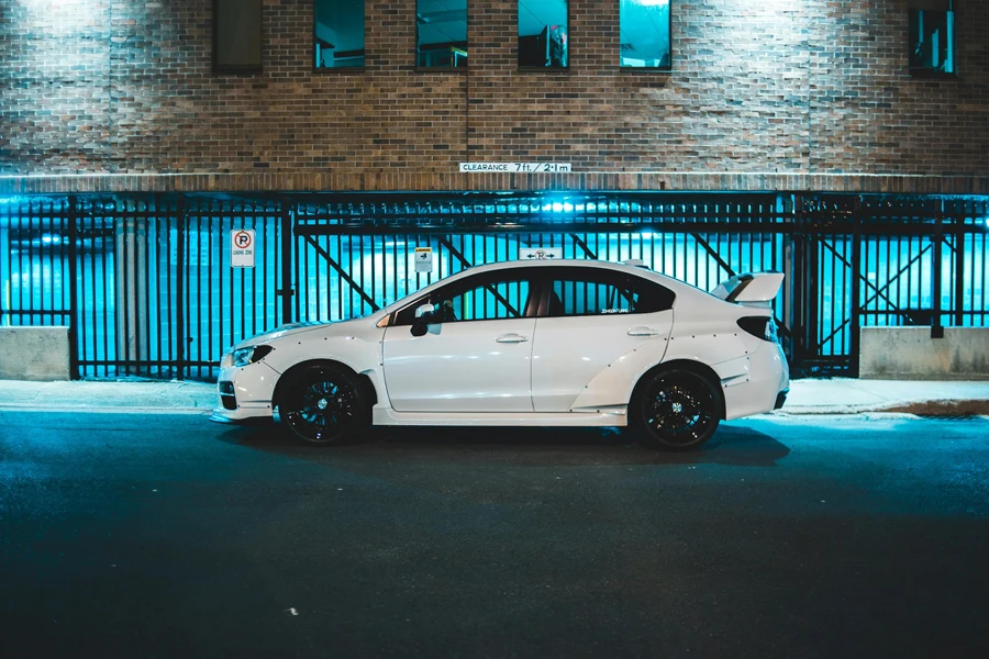 Modern automobile with black wheels and shiny white body on asphalt road near brick building behind fence