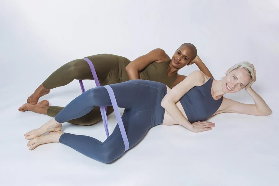 Multiracial ladies lying and doing exercises with resistance loops