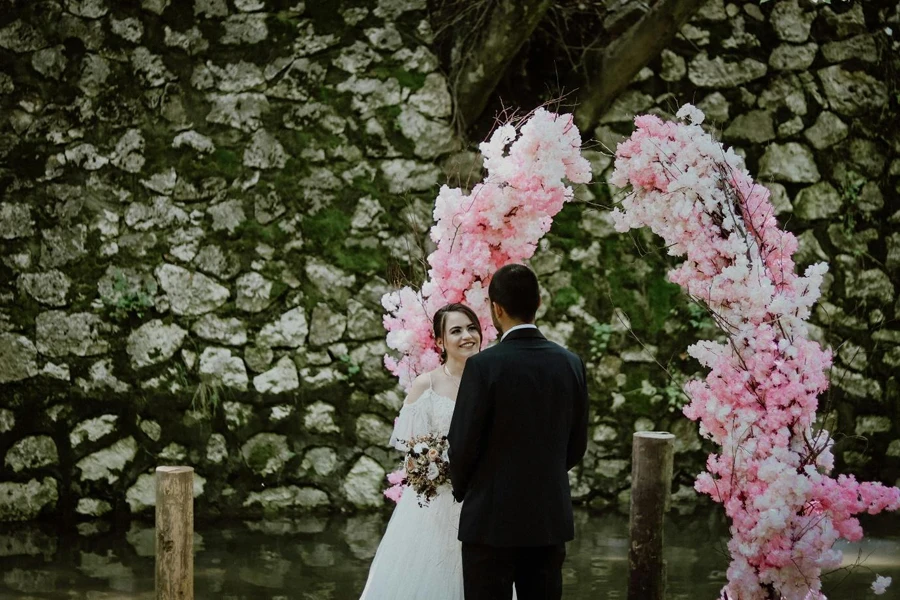 花のアーチの近くで結婚する男女の写真